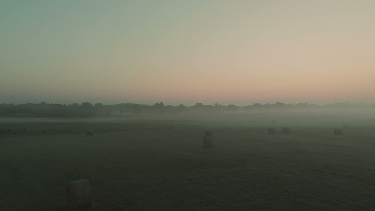 Misty dawn over the Ozark ranch, hay bales dotting a sprawling pasture beneath a golden sunrise